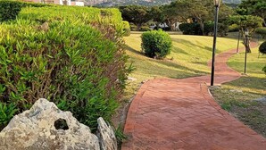 A paved pathway leading to a building with a mountain backdrop. - Porto Cervo Cala del Faro rent BILOCALE garden porch near the sea. (Porto Cervo)
