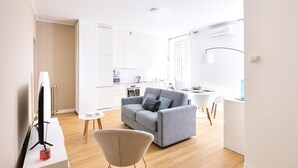 Ett modernt vardagsrum med en grå soffa, ett litet bord och en tv som står på ett vitt tv-bord.