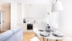 Ett modernt kök med vita köksskåp, ett matbord dukat med tallrikar och glas, och en ljus soffa i förgrunden.