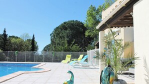 En swimmingpool med en statue af en påfugl, liggestole og en stor plantekasse med et palmetræ.