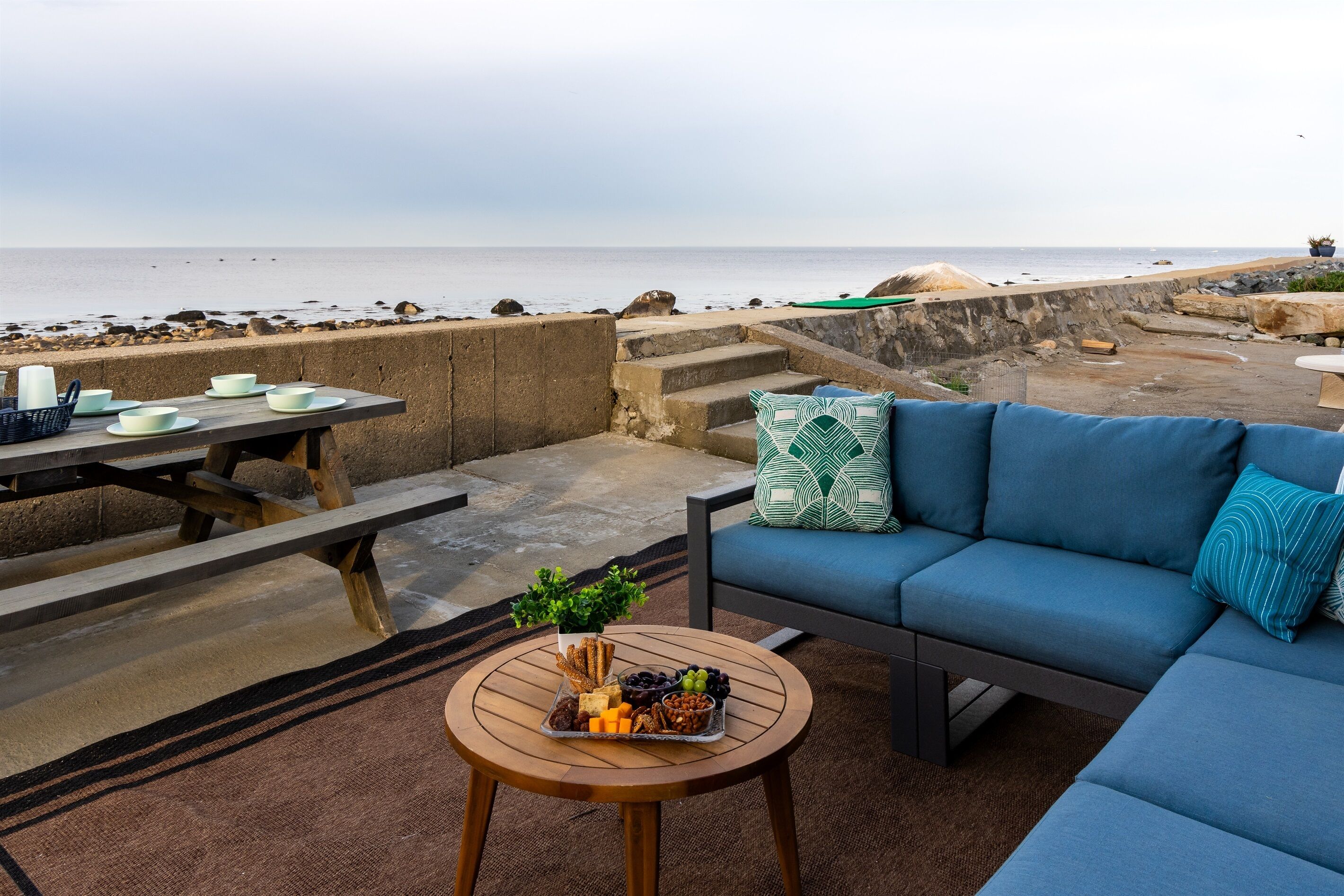 Ein Außenbereich mit Meerblick, ein Tisch mit Snacks und ein blaues Sofa.