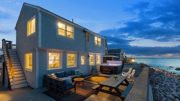 A two-story house with a patio area featuring a hot tub, seating, and a view of the ocean. - Oceanfront home w/Amazing Views, Hottub! Sleeps 10 (Scituate)