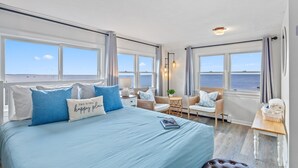 A bedroom with a large bed, two windows with ocean views, a small table, and a chair. - Oceanfront home w/Amazing Views, Hottub! Sleeps 10 (Scituate)