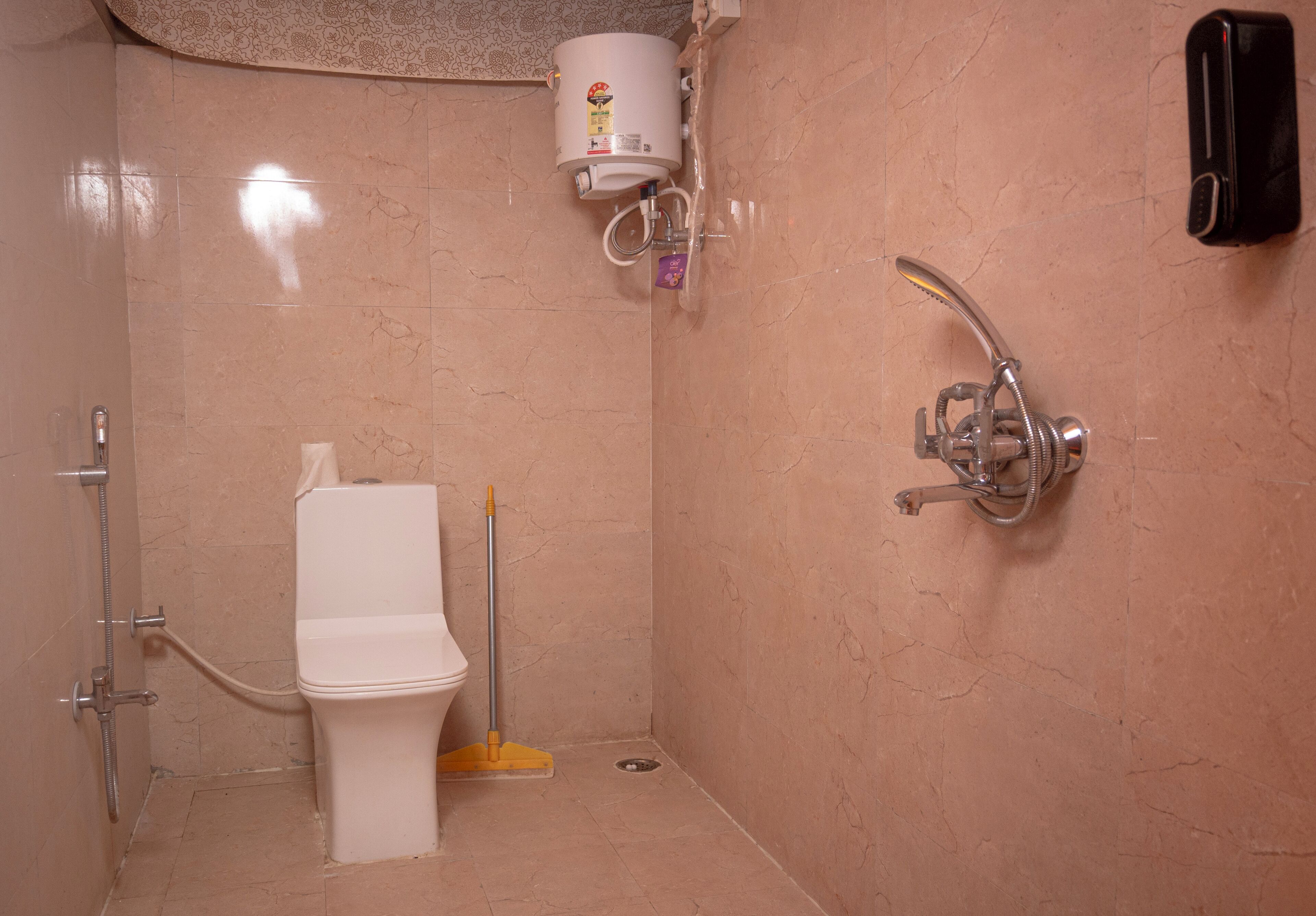 A bathroom with a toilet, a handheld showerhead, a wall-mounted faucet, and a soap dispenser.