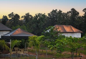 A rustic outdoor setting with a covered seating area, a small building, and lush greenery. -  Bundeli Camps and Resorts, Panna (Panna)