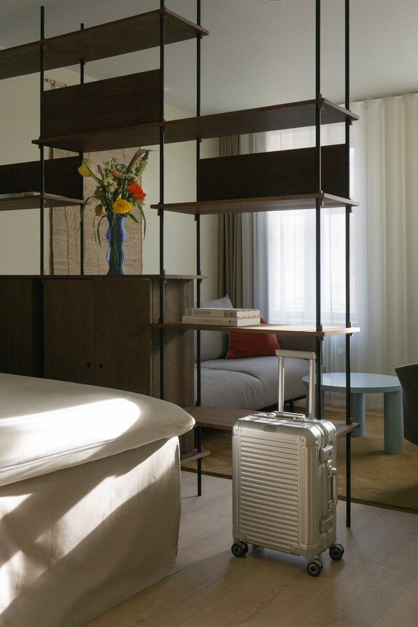 Une chambre d’hôtel avec un lit, un bureau, une valise et une étagère sur laquelle se trouve un vase de fleurs.