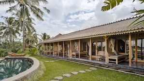 A poolside area with a covered seating area, stone pathway, and lush greenery.