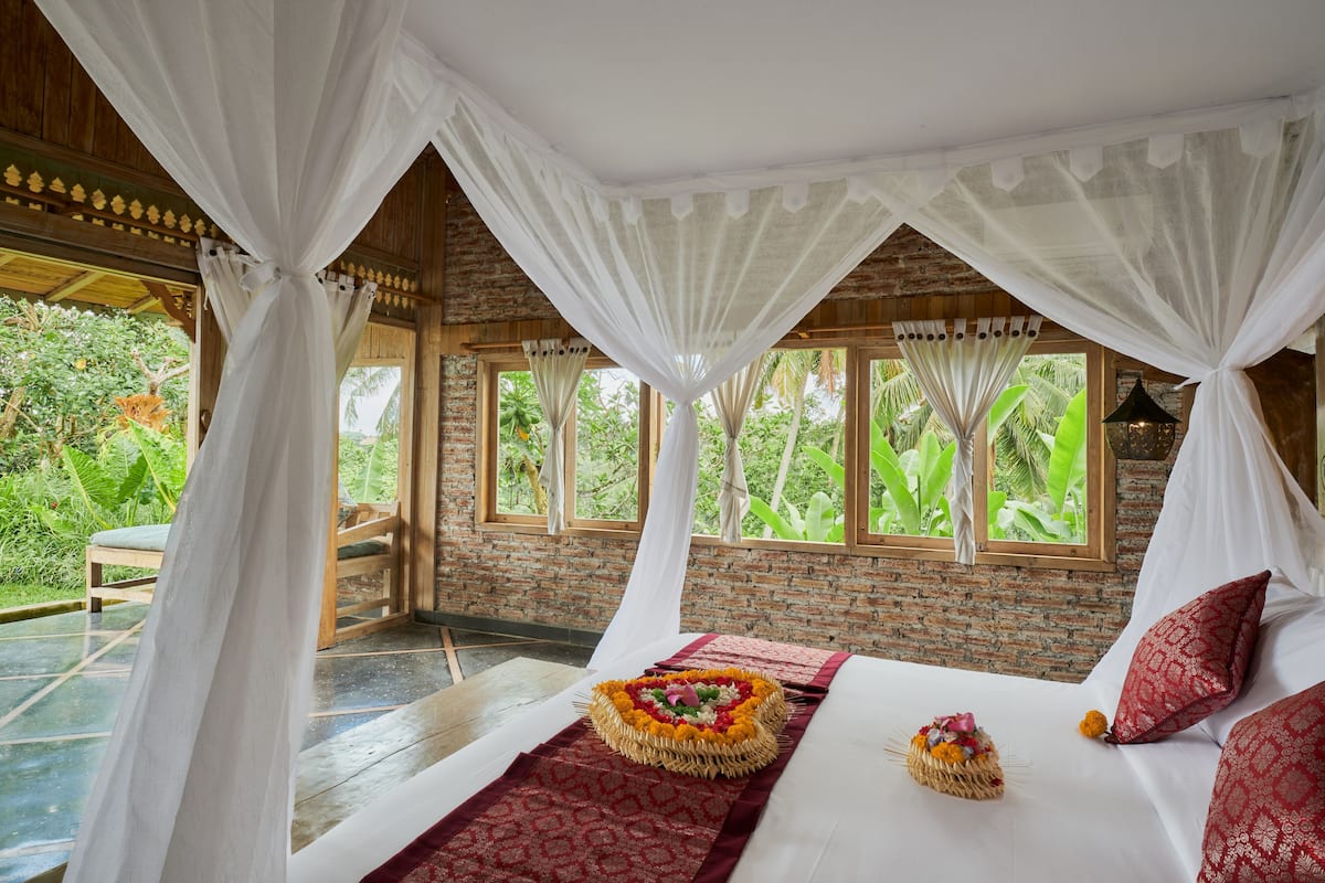 Una habitación con una cama, un tapete de zona rojo con estampado y una cama con dosel y cortinas blancas.