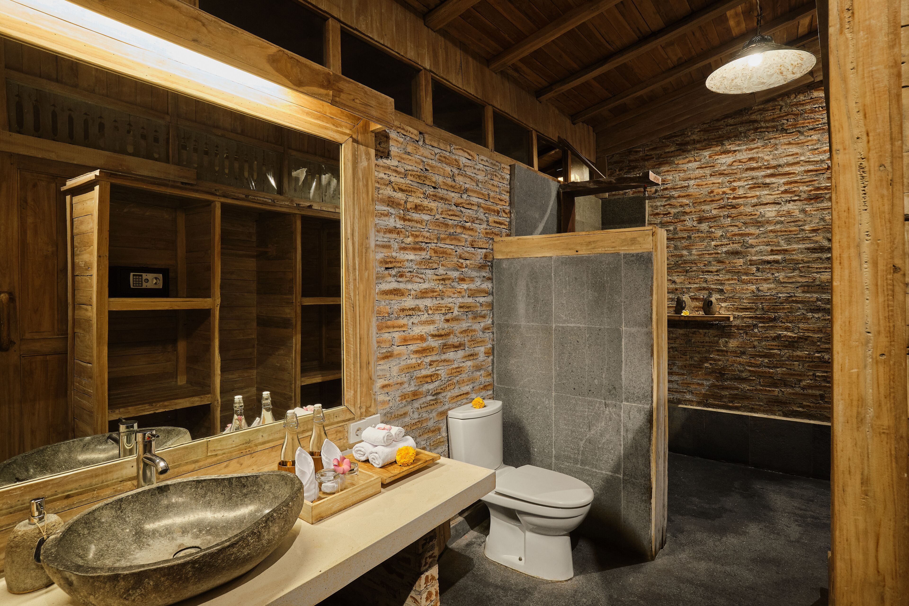 A rustic bathroom with a stone sink, wooden vanity, and a white toilet.