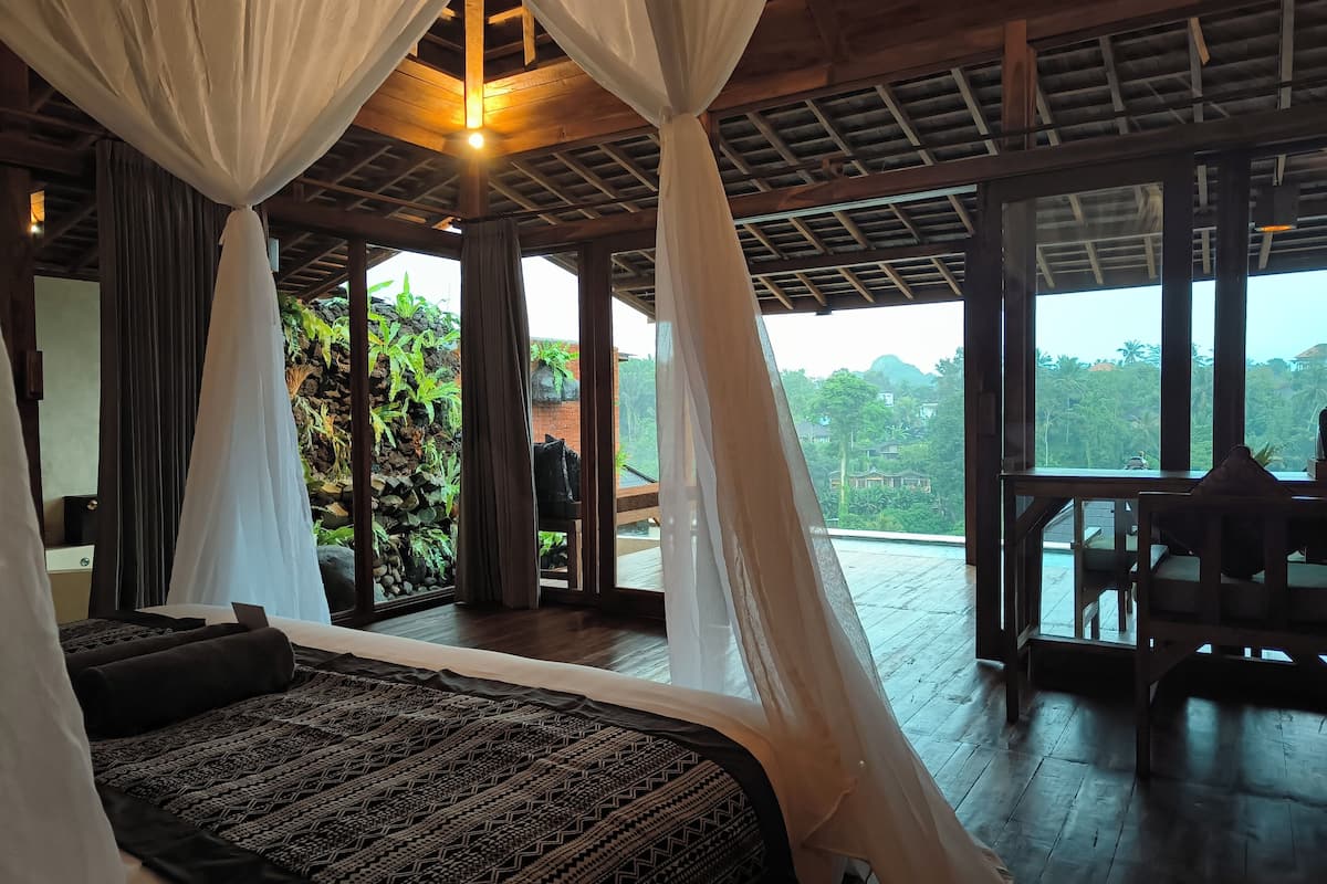 Un dormitorio con una cama grande, techo de madera y vistas a exuberante vegetación.