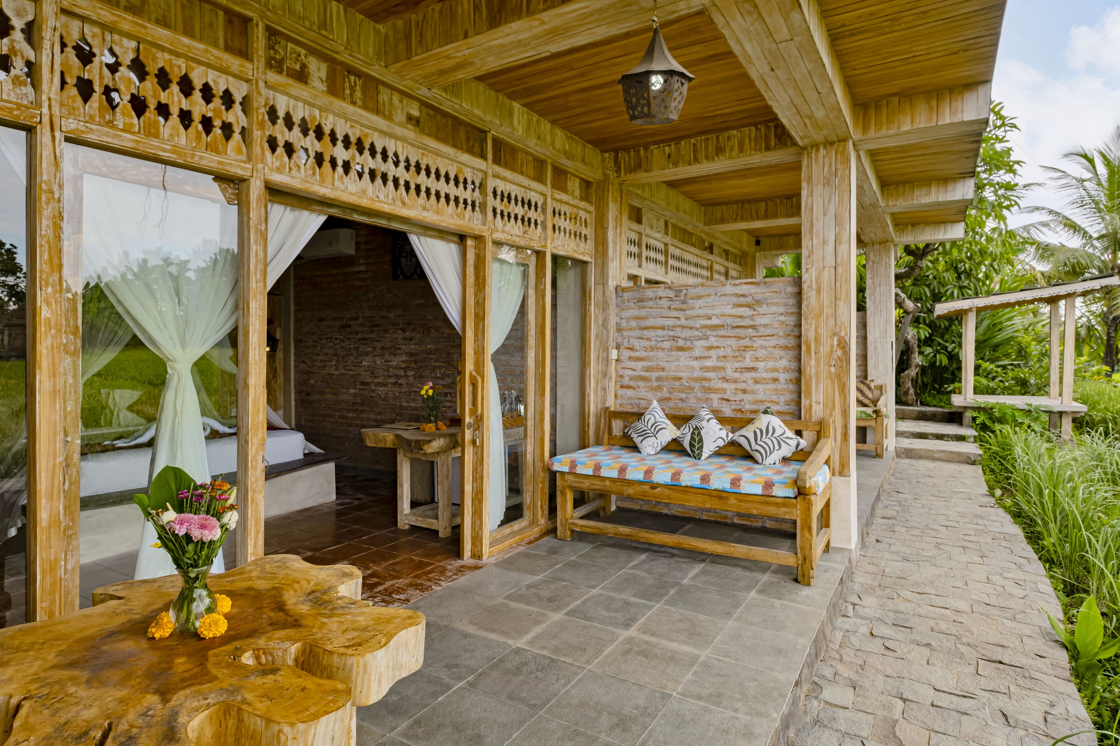 A wooden veranda with a bench and a table with a vase of flowers.