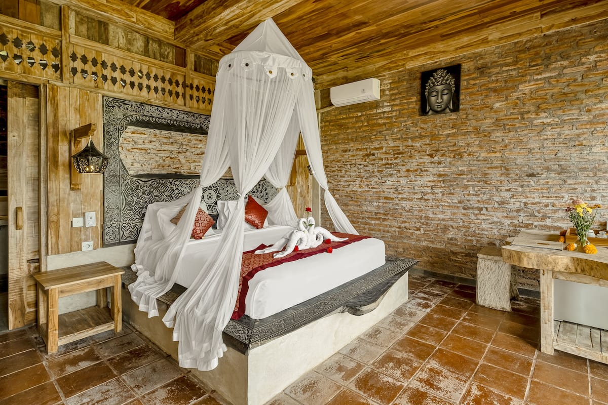 Una habitación con cama, una mesita pequeña, aire acondicionado instalado en la pared y un cabecero decorativo.