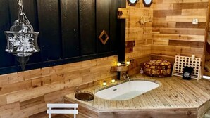 A wooden interior with a large bathtub, a hanging light fixture, and a small table with candles.
