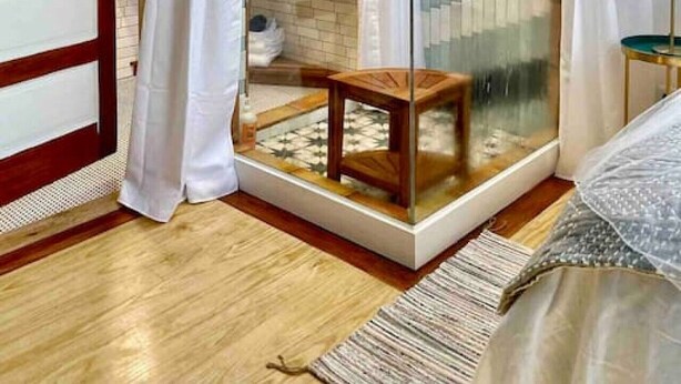 A modern bathroom with a glass shower enclosure, wooden beams, and a tiled floor.