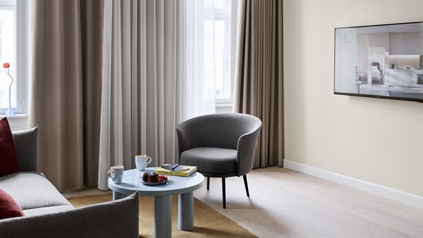 A modern hotel room with a grey armchair, a round coffee table with a book and a plate of food, and a large window with curtains. - One-Bedroom Apartment for 6 with Open Plan (København)