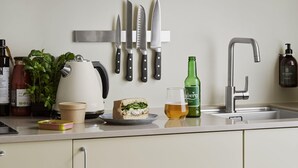 A kitchen with a white countertop, a kettle, a sandwich, a glass of beer, a bottle of beer, and several knives hanging on the wall. - One-Bedroom Apartment for 6 with Open Plan (København)