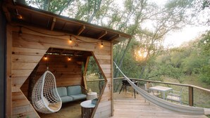 A wooden deck with a hammock, a hanging chair, and a table with chairs. - Sapling Treehouse at HoneyTree (Fredericksburg)