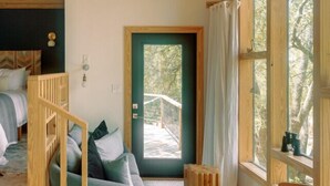 A cozy room with a bed, a sofa, a small table, and a window with a view of trees. - Sapling Treehouse at HoneyTree (Fredericksburg)