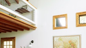 A room with a wooden floor, a dining table with chairs, a large potted plant, and a painting on the wall. - Sycamore Treehouse at The Meadow by HoneyTree (Fredericksburg)