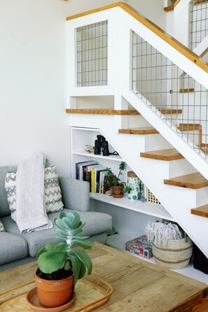Un salon moderne avec un canapé gris, une table basse ornée d’une plante en pot et un escalier blanc avec des marches en bois et des rampes en métal.