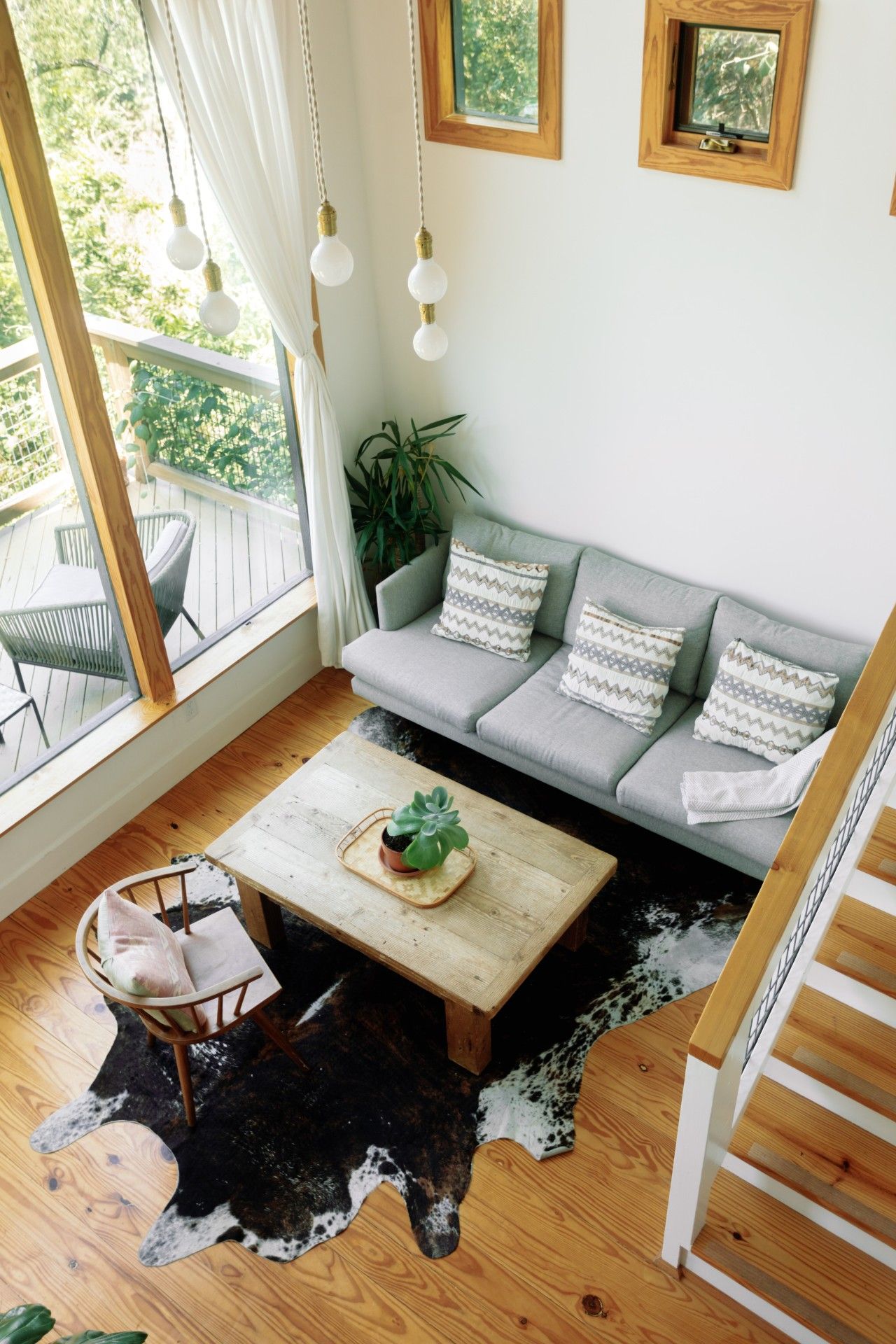 Una sala de estar moderna con un sofá gris, cojines estampados, una mesa de centro de madera, un tapete de cuero de vaca y una escalera.