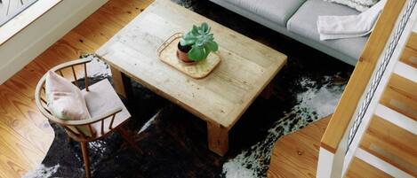 Una sala de estar moderna con un sofá gris, cojines estampados, una mesa de centro de madera, un tapete de cuero de vaca y una escalera.
