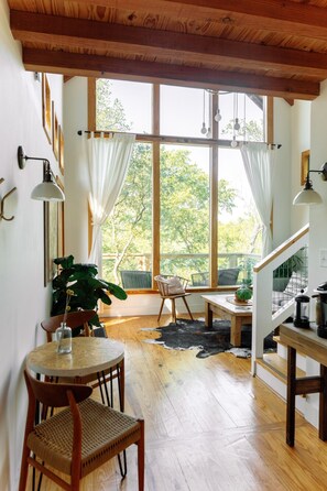 Un intérieur chaleureux avec un coin repas, un plancher en bois et de grandes fenêtres donnant sur un paysage verdoyant.