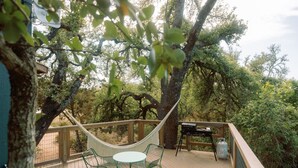 A wooden deck with a hammock, chairs, and a barbecue grill. - Sycamore Treehouse at The Meadow by HoneyTree (Fredericksburg)