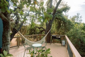 Une terrasse en bois avec un hamac, des chaises et un barbecue.