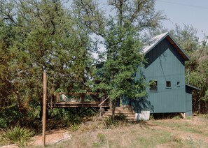 Une cabane rustique dotée d’une terrasse en bois et d’un toit en métal, entourée d’arbres et de végétation.