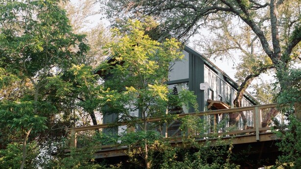 A house with a wooden deck and a staircase leading to a balcony. - Sycamore Treehouse at The Meadow by HoneyTree (Fredericksburg)