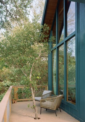 A covered outdoor seating area with wicker chairs and a wooden deck. - Sycamore Treehouse at The Meadow by HoneyTree (Fredericksburg)