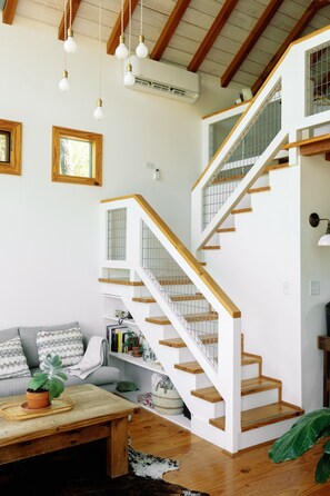 A staircase with wooden steps and white railings, a wooden bench with a potted plant, and a wall-mounted air conditioning unit. - Sycamore Treehouse at The Meadow by HoneyTree (Fredericksburg)