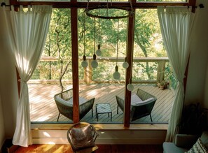 Une pièce donnant sur une terrasse en bois, meublée de mobilier en osier et agrémentée d’un luminaire suspendu.