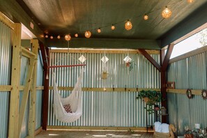 A rustic interior with a hammock, hanging lights, and a corrugated metal wall.