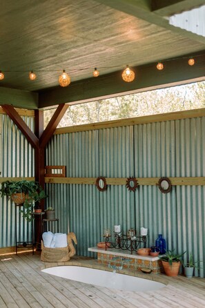 A covered outdoor area with a wooden floor, corrugated metal walls, and a ceiling with hanging lights. - Live Oak Treehouse at The Meadow (Fredericksburg)