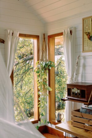A room with a bed, a wooden table, a radio, and a window with curtains.