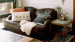A cozy room with a brown leather sofa, a small wooden table, and a window with a curtain.