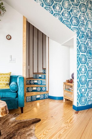 Un salón moderno con un sofá azul, escalera de madera y paredes con diseños.