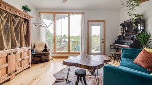 A spacious living room with a wooden cabinet, a blue sofa, a round coffee table, and a piano.