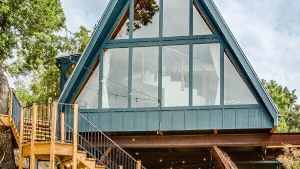 A modern, triangular-roofed building with large windows, wooden stairs, and outdoor seating. - Blue Sage No. 2 - The Floating A-Frame (Fredericksburg)