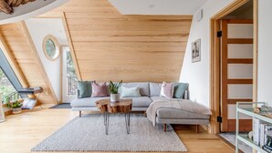 A modern living room with a wooden ceiling, a grey sectional sofa, a wooden coffee table, and a bookshelf. - Blue Sage No. 2 - The Floating A-Frame (Fredericksburg)