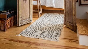 Ein gemütliches Schlafzimmer mit schrägen Wänden, Holzbalken, einem Bett mit weißen Leinen, einem kleinen Tisch und einem Teppich.