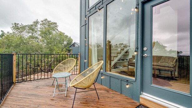 Una terraza de madera con dos sillas de mimbre, un ventanal y vista al interior.