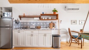 Une cuisine moderne avec des armoires blanches, un réfrigérateur en acier inoxydable, un four à micro-ondes et un grille-pain. Une étagère en bois, située au-dessus du plan de travail, sert à ranger la vaisselle et une plante en pot.