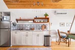 A modern kitchen with white cabinets, a stainless steel refrigerator, a microwave, and a toaster. There is a wooden shelf above the countertop holding dishes and a potted plant. - Blue Sage No. 6 - The Long View Treehome (Stair-Free!) (Fredericksburg)
