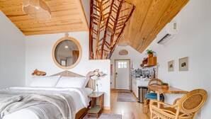 Une chambre avec un plafond en bois, un miroir rond, un lit avec une literie blanche, une petite table et une chaise.