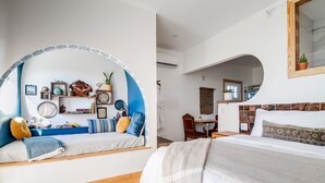 Una habitación con dos camas, un arco azul, suelo de madera y un escritorio pequeño con una silla.