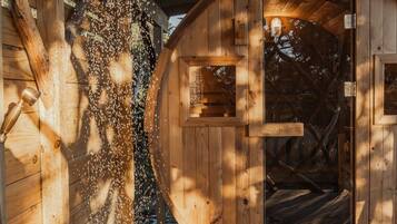Eine Holzhütte mit einer runden Tür, einer Duschgelegenheit und einer Holzdielen-Terrasse.