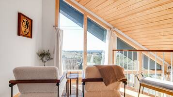 A room with two chairs, a table, and a view through large windows.